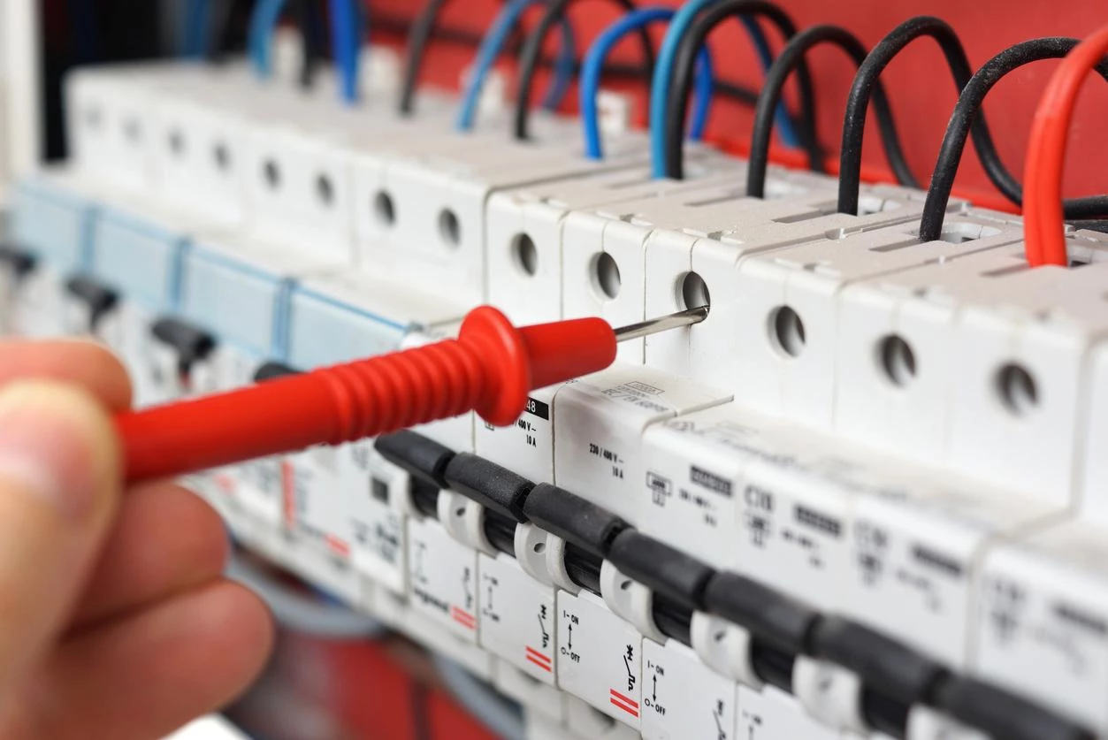 An electrician fixing an electrical switchgear cabinet with a multimeter probe.