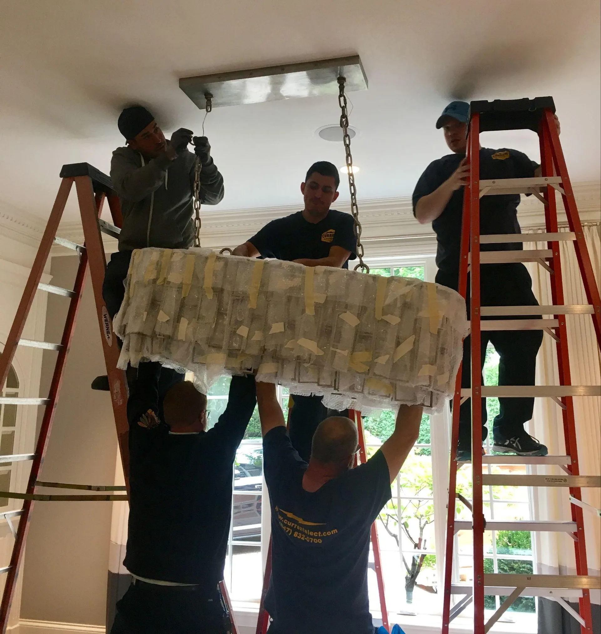 Electrical contractors in Mount Prospect, IL, installing a chandelier